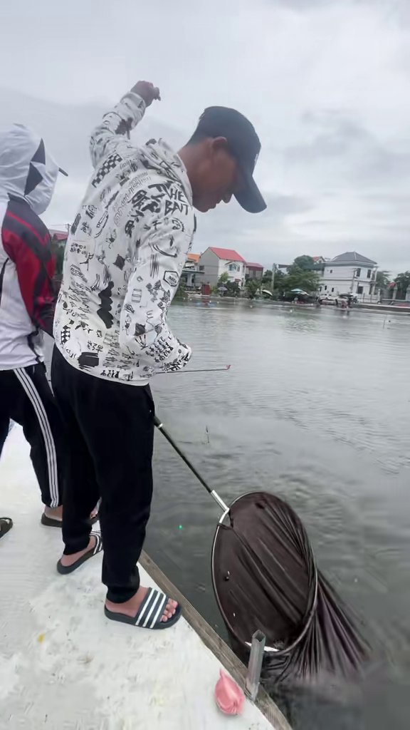 Người đàn ông đang câu cá, hạ rọng lưới xuống nước trên sàn.
